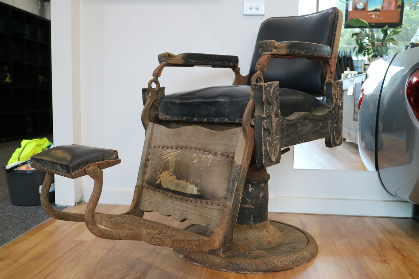 Antique barber chair with rusted iron footrest and worn black leather on display in the shop