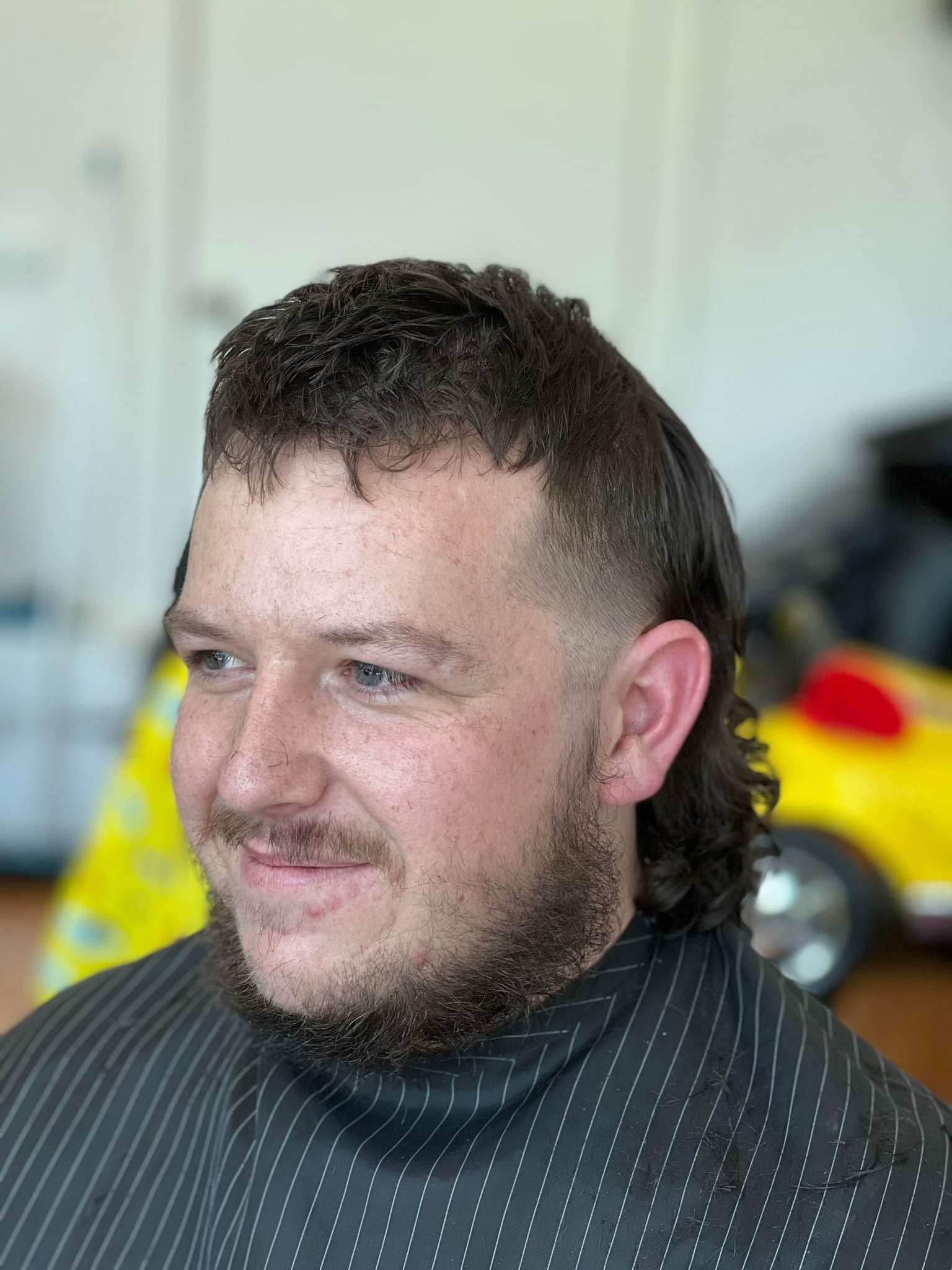 Customer with a fresh mullet and beard, a yellow kids' car seat behind him